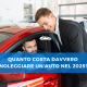 Un consulente auto in giacca nera sorride mentre assiste un cliente seduto all'interno di un’auto rossa in una concessionaria moderna. In sovrimpressione, un banner blu con la scritta: “Quanto costa davvero noleggiare un’auto nel 2025?”.